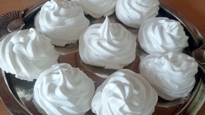 Baiser mit hoher, geschwungener Form liegen auf einem silbernen Tablett, umgeben von einer hellen Holzoberfl&auml;che.