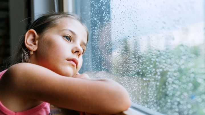 Ein M&auml;dchen blickt nachdenklich aus dem Fenster, w&auml;hrend es regnet, und wirkt dabei traurig und entt&auml;uscht.