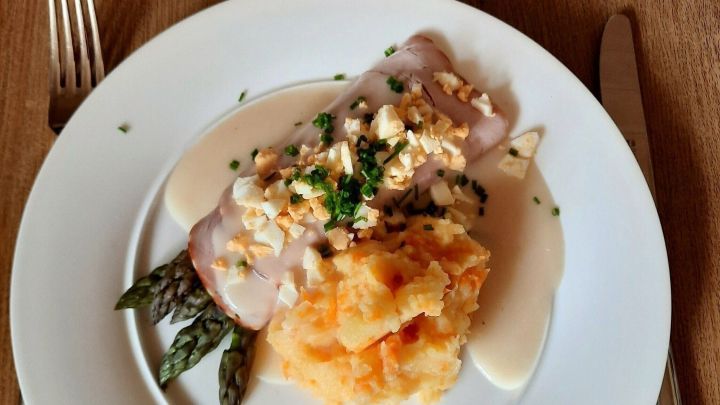 Gr&uuml;ner Spargel liegt auf einem Teller, bedeckt mit leichter So&szlig;e, neben Kartoffel-Karotten-Stampf auf einem Tisch.