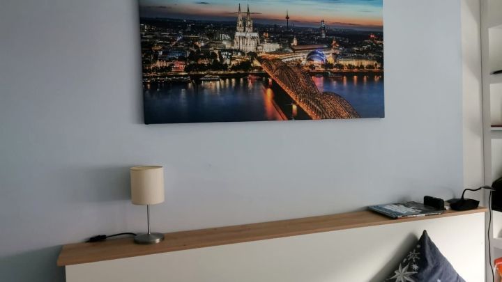 Ein Lampenst&auml;nder steht auf einem Brett hinter einem Bett, mit einer Stadtansicht &uuml;ber einem ruhigen Schlafzimmer.