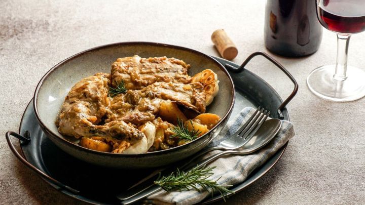 Ein Teller mit Kaninchen in Salmorejo, serviert mit Kartoffeln und einem Glas Rotwein auf einem rustikalen Tisch.