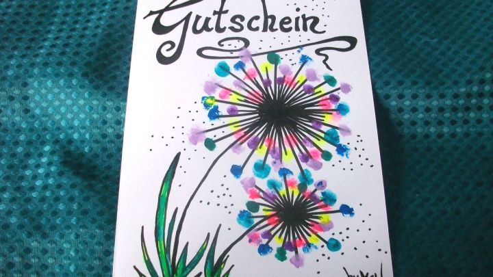 Eine kreative Gutscheinkarte zeigt bunte Blumen mit dem Text &bdquo;Gutschein&ldquo; auf einem schimmernden Hintergrund.