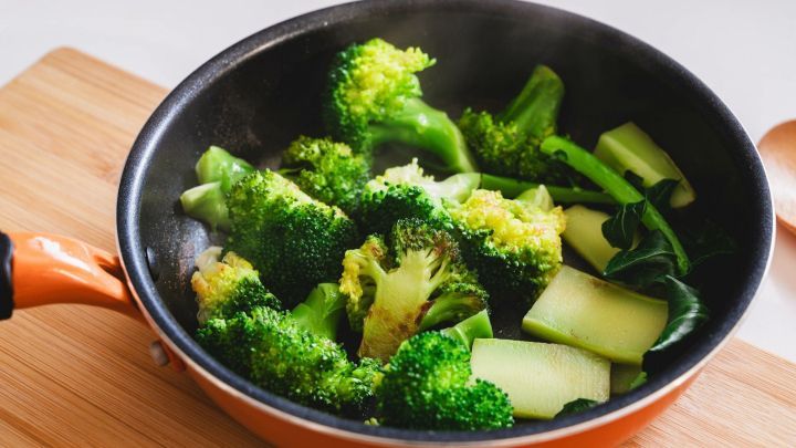 Brokkoli und Gem&uuml;se werden in einer Pfanne ged&auml;mpft, auf einem Holzbrett in einer modernen K&uuml;che mit heller Umgebung.