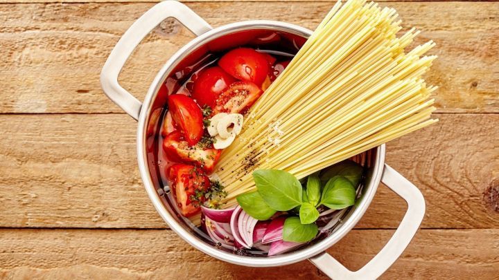 Ein Topf mit frischen Tomaten, Zwiebeln, Basilikum und Spaghetti wird f&uuml;r ein einfaches One-Pot-Gericht vorbereitet.