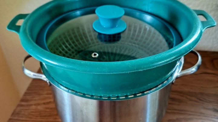 Ein Edelstahlkochtopf mit einem gr&uuml;nen Dampfgareinsatz steht auf einem Holztisch, bereit zum Dampfgaren ohne Dampfgarer.