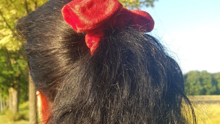 Dunkles, lockiges Haar wird von einer Person mit einem roten Haargummi im Freien getragen, umgeben von Natur.