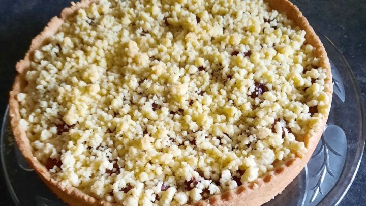 Der runde Kirsch-Streuselkuchen mit Schmand ruht auf einer Glasplatte mit Blattmuster.