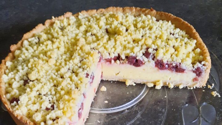 S&uuml;&szlig;er Kirsch-Streuselkuchen mit einer goldenen Kruste und einer schmalen Schnittkante auf einem eleganten Glassicht.