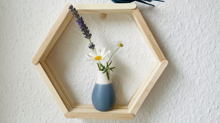 Ein Mini-Hexagon-Regal aus Holz zeigt eine kleine Vase mit Blumen und wird von einem dekorativen Vogel begleitet.