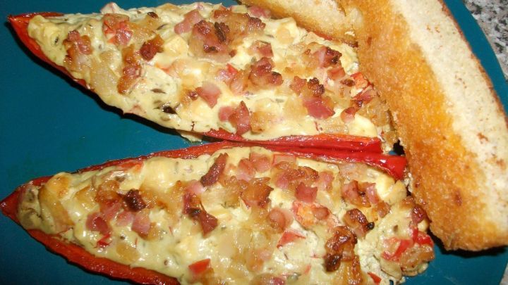 &Uuml;berbackene Paprika f&uuml;llen mit Hirtenk&auml;se und Speck liegen auf einem Teller, umgeben von ger&ouml;stetem Brot.