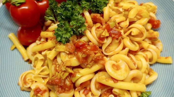 Eine Teller Sommerpasta mit Knoblauch und Tomaten, garniert mit frischem Petersilie und Kirschtomaten, auf einem blauen Teller.