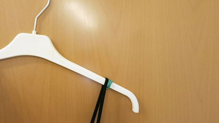 Ein Kleiderb&uuml;gel h&auml;lt ein Tr&auml;gerkleid mit einem Gummiband, um ein Herunterrutschen zu verhindern, vor einer Holzoberfl&auml;che.