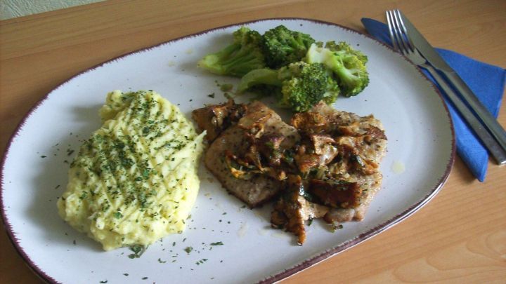 Saftiges Kalbfleisch liegt zusammen mit cremigem Kartoffelp&uuml;ree und Brokkoli auf einem Teller in einer gem&uuml;tlichen K&uuml;che.