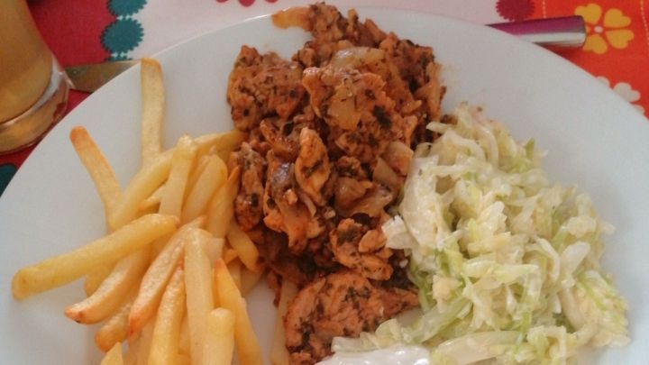 Saftiges Gyros mit Tsatsiki liegt auf einem wei&szlig;en Teller, umgeben von Pommes und frischem Salat, auf buntem Tisch.