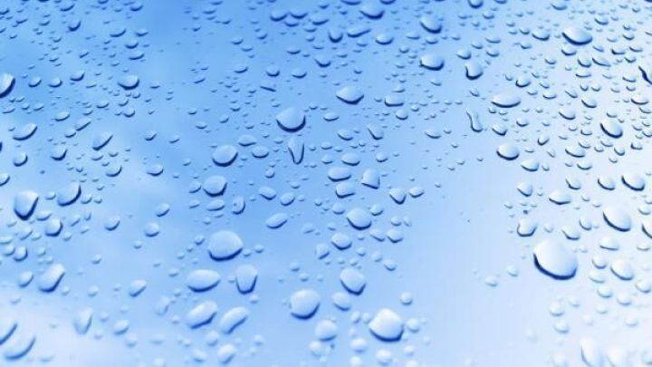 Wassertropfen bilden sich auf einer glatten Oberfl&auml;che, die mit Autowachs versiegelt wurde, glitzernd im blauen Licht.