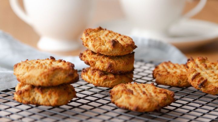 Kekse ohne Zucker stehen auf einem Gitter, w&auml;hrend wei&szlig;e Tassen im Hintergrund eine gem&uuml;tliche Teestunde ank&uuml;ndigen.