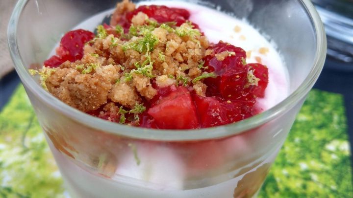 Ein glasiges Erdbeertrifle mit frischen, roten Erdbeeren, knusprigen Br&ouml;seln und einer sahnigen Schicht auf gr&uuml;nem Untergrund.