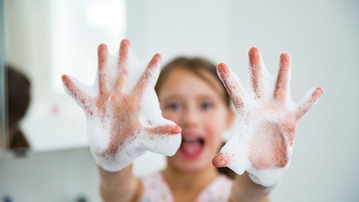 Ein fr&ouml;hliches Kind zeigt stolz seine sch&auml;umenden H&auml;nde, w&auml;hrend es in einer hellen Badezimmerumgebung mit Seife spielt.