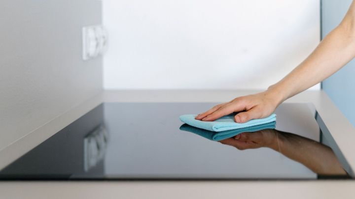 Ein Hand wischt mit einem blauen Tuch &uuml;ber ein gl&auml;nzendes Ceranfeld in einer modernen K&uuml;chenumgebung.