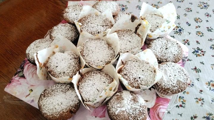 Auf einem Kuchenstand liegen viele frisch gebackene Prager-Schokoladen-Nussmuffins, mit Puderzucker best&auml;ubt.