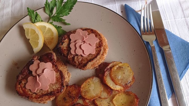 Zwei Kalbsfilets auf einem Teller, dekoriert mit rosa Schinken, umgeben von Kartoffelscheiben und Zitronenscheiben.