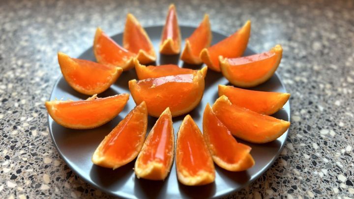 Auf einem grauen Teller sind mit Aperol gef&uuml;llte Jelly Shots in der Form von Orangenschnitzen angeordnet.