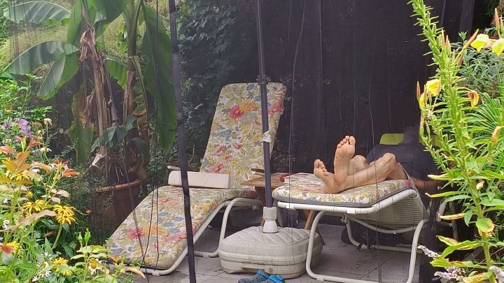 Eine gem&uuml;tliche Liegefl&auml;che unter einem Moskitonetz, w&auml;hrend sich jemand entspannt im Garten umgeben von Pflanzen.