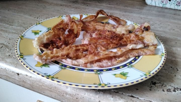 Knuspriger Bacon liegt auf einem bunten Teller und verstr&ouml;mt appetitliches Aroma in einer hellen K&uuml;chenumgebung.