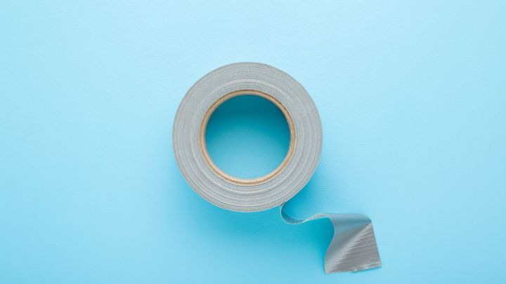 Ein graues Klebeband rollt leicht ab auf einem hellblauen Hintergrund.