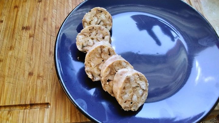 Brezenkn&ouml;del-Scheiben liegen auf einem schwarzen Teller, der auf einem Holzbrett steht. Es gibt keinen Text im Bild.