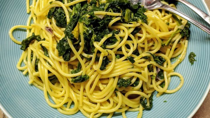 Spaghetti mit Spinat liegt auf einem blauen Teller, daneben liegt Besteck. Sie sind gelblich und dampfen leicht auf.