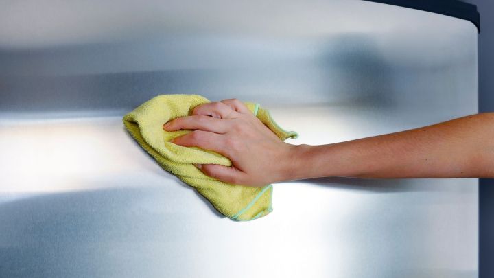 Eine Hand reinigt mit einem gelben Tuch sanft eine Edelstahloberfl&auml;che, vermutlich einen K&uuml;hlschrank, in einem modernen Raum.