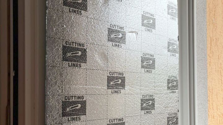 Alu-Trittschalld&auml;mmung bedeckt ein Fenster erkennbar an aufgedruckten &bdquo;CUTTING LINES&ldquo; und reflektiert Licht im Innenbereich.