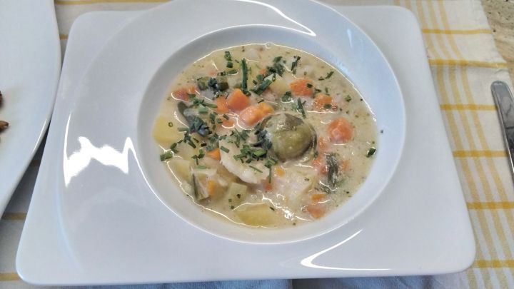 Eine Gem&uuml;sesuppe in einem wei&szlig;en Teller zeigt viele bunte Gem&uuml;sew&uuml;rfel und Kr&auml;uter, serviert auf einem karierten Tuch.