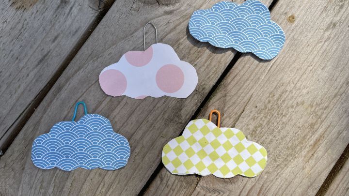 Papierwolken mit bunten Mustern h&auml;ngen an B&uuml;roklammern auf einem Holztisch.