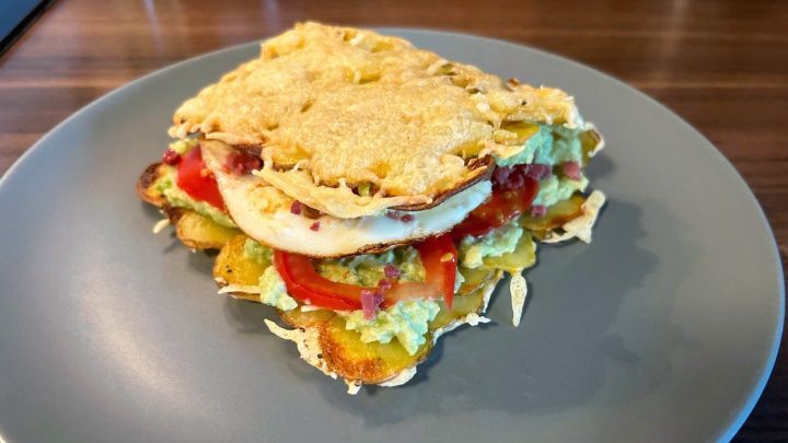 Ein Kartoffel-K&auml;se-Sandwich mit Avocado und Tomaten liegt auf einem grauen Teller in einer K&uuml;che.