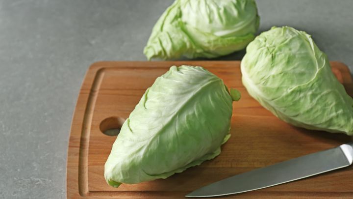 Spitzkohl liegt auf einem Holzbrett, bereit zum Schneiden mit einem Messer, in einer K&uuml;chenumgebung.