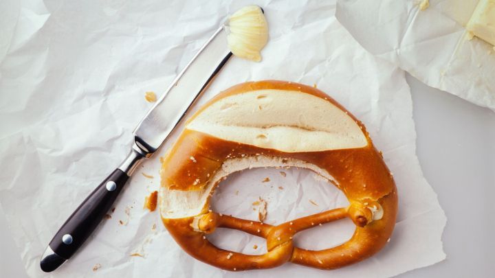 Butterbrezel auf Papier, daneben ein Messer mit Butter, umgeben von kleinen Kr&uuml;meln.