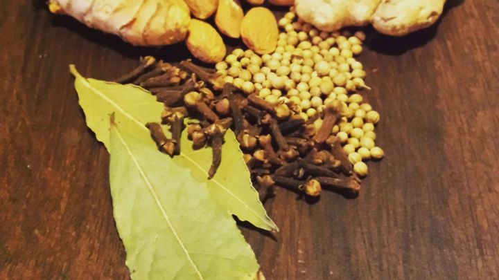 Gew&uuml;rze wie Lorbeerbl&auml;tter, Nelken, Kurkuma, Mandeln, Korianderk&ouml;rner und Ingwer liegen ordentlich auf einem Holztisch.