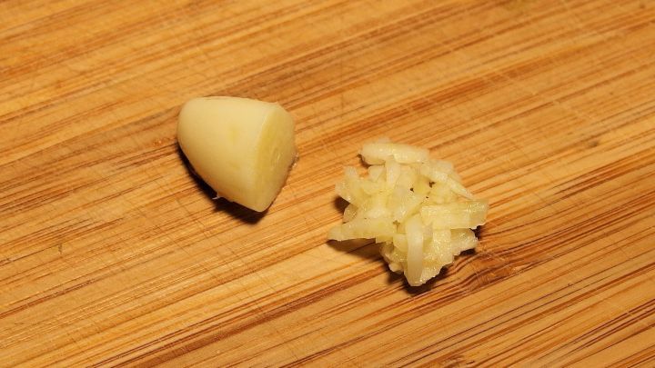 Ein Knoblauchzehe liegt neben zerdr&uuml;cktem Knoblauch auf einem Holzbrett, optimal zur Bek&auml;mpfung von Fu&szlig;pilz und Nagelpilz.