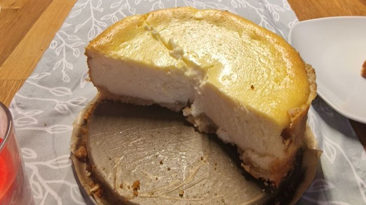 Der K&auml;sekuchen steht auf einem Tisch, wobei ein St&uuml;ck herausgeschnitten ist, um ihn zu servieren. Der Tisch ist klar gedeckt.