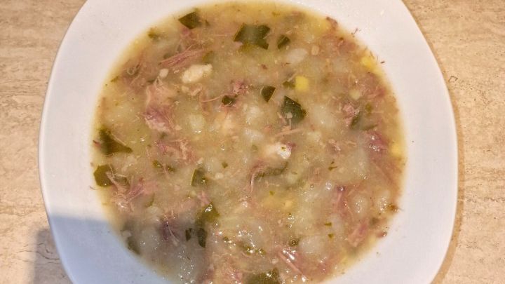 Ein wei&szlig;er Teller mit cremigem Kohlrabieintopf auf einem beigen Tisch. Der Eintopf enth&auml;lt gr&uuml;ne Kr&auml;uter und Fleischst&uuml;cke.