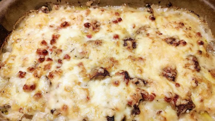 Kn&ouml;delauflauf in einer Backform, &uuml;berbacken mit K&auml;se, zeigt eine br&auml;unlich-goldene Kruste und verteilt liegende Pilzst&uuml;cke.