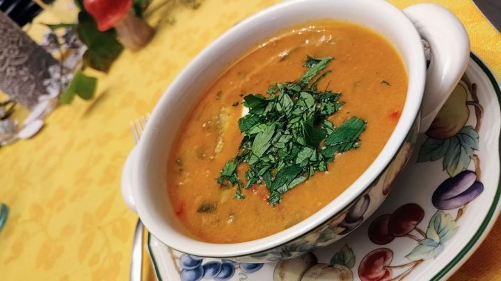 Eine bunte Sch&uuml;ssel Fischsoljanka steht auf einem Tisch, garniert mit frischem Koriander, umgeben von einer freundlichen Atmosph&auml;re.