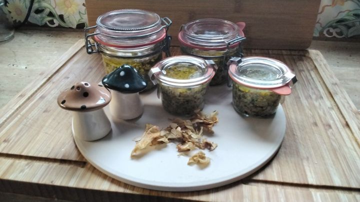 Gl&auml;ser mit Steinpilz-Pesto stehen auf einem Holzbrett, umgeben von getrockneten Pilzen und kleinen Pilzen.