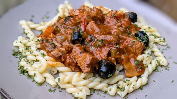 Pasta serviert mit saftiger Pute, Tomatenso&szlig;e und schwarzen Oliven auf einem Teller, garniert mit Petersilie.