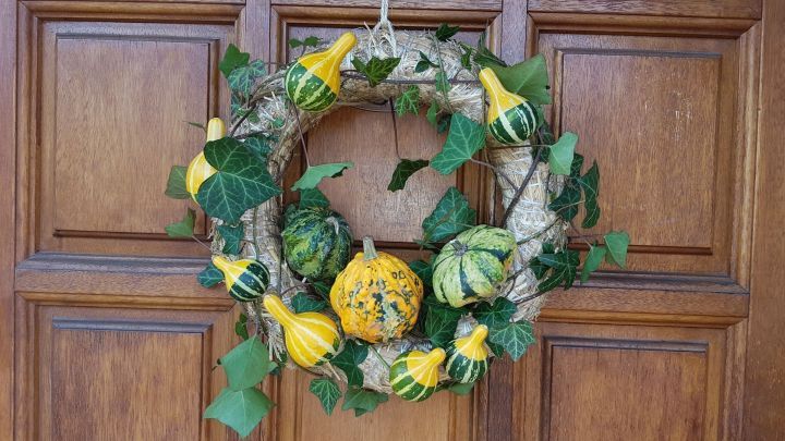 Ein T&uuml;rkranz mit Zierk&uuml;rbissen und gr&uuml;ner Efeu-Ranken schm&uuml;ckt eine Holzhaust&uuml;r und verleiht eine herbstliche Atmosph&auml;re.