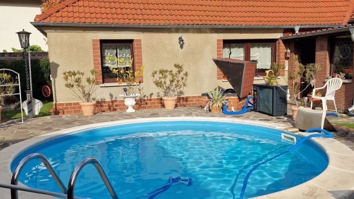 Ein runder Pool mit klarem Wasser steht vor einem Haus, umgeben von bunten Herbstlaub und einer Terrasse mit Gartenm&ouml;beln.