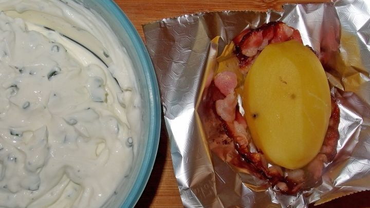 Auf einem Tisch liegt eine Folienkartoffel mit Schinken, daneben eine Sch&uuml;ssel mit cremigem Dip.
