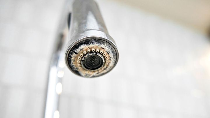 Ein stark verkalkter Perlator an einem Wasserhahn in einer hell gefliesten Umgebung ben&ouml;tigt dringend Entkalkung.